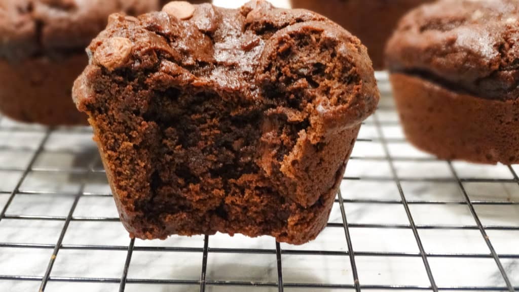 alt="double chocolate bakery style muffins with chocolate chips on a cooling rack"