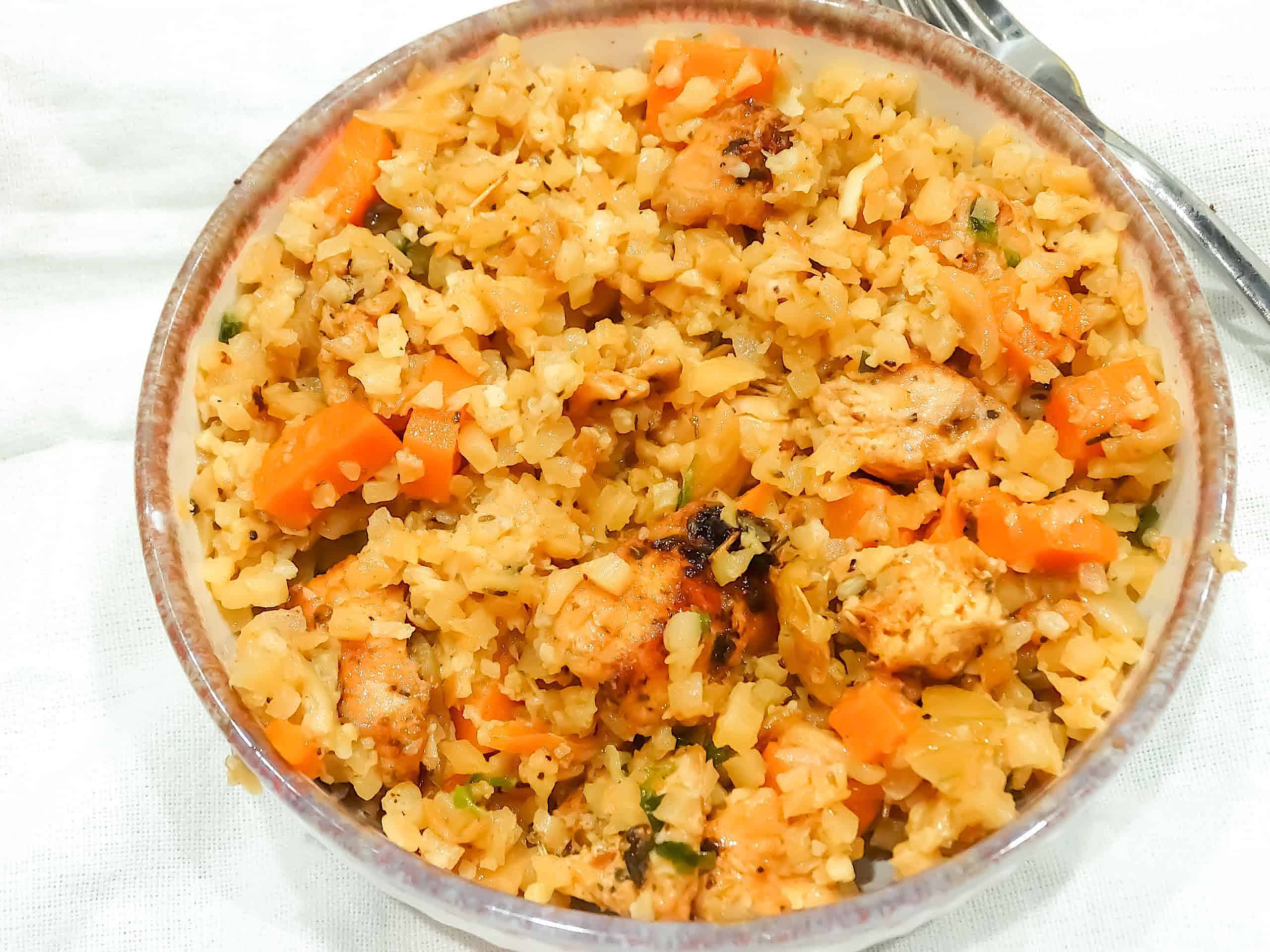 cauliflower rice stir fry with garlic butter chicken, carrots, and parsley in a white bowl