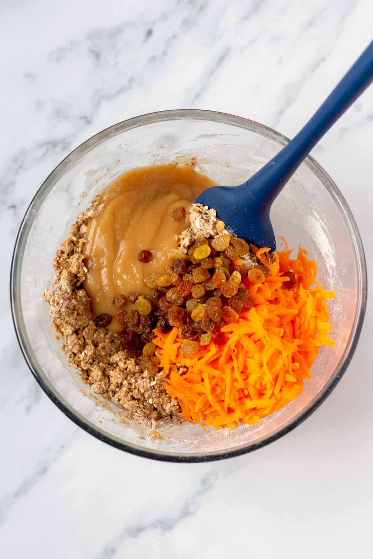 carrots and raisins added to muffin batter in a mixing bowl