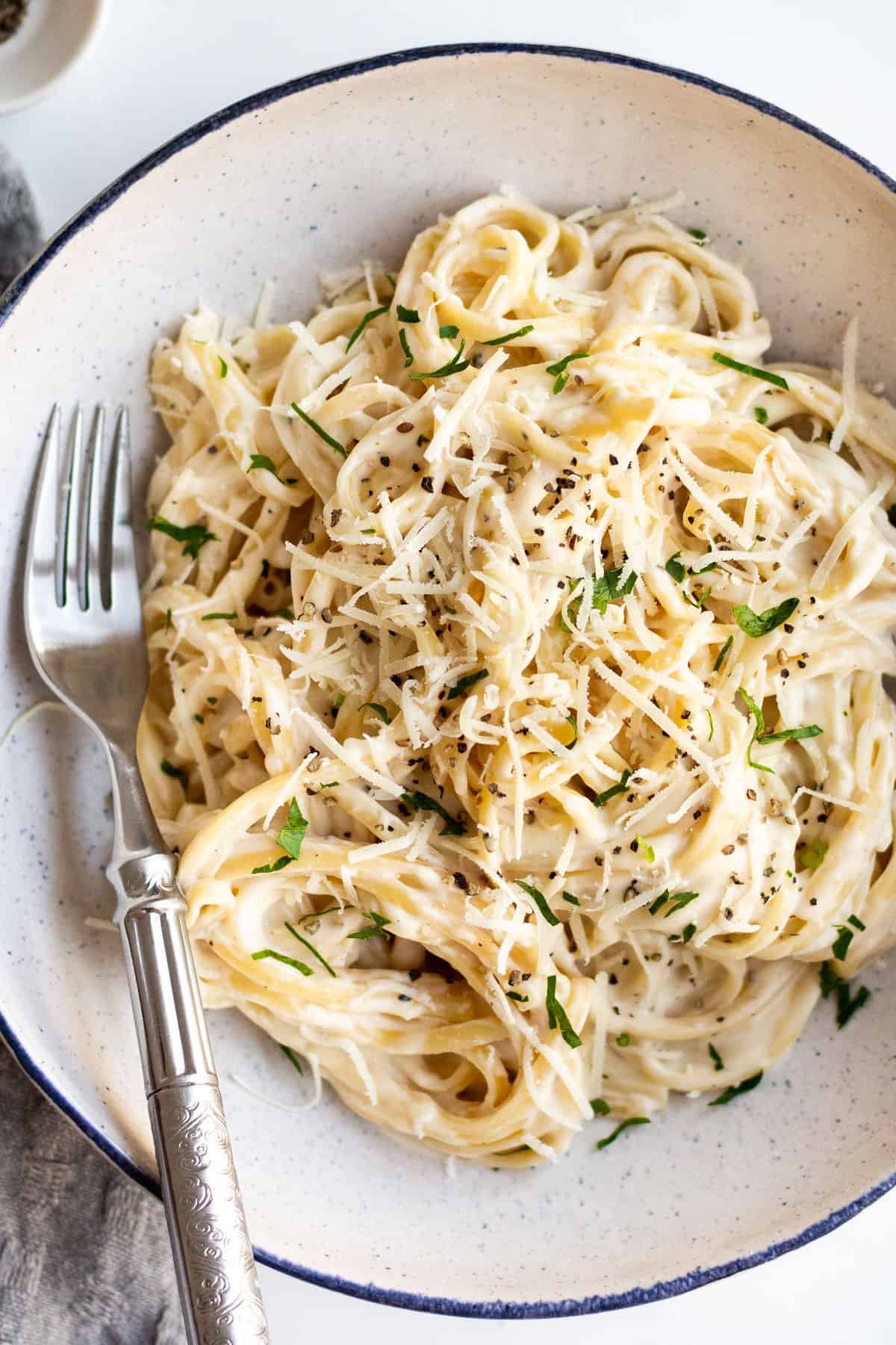 white pasta sauce tossed with noodles in a white bowl