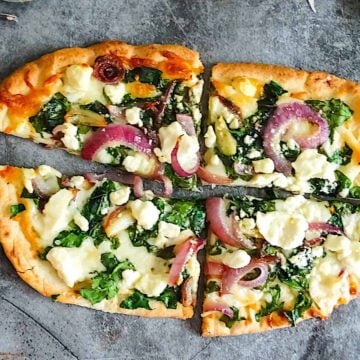 spinach and feta flatbread pizza cut into 4 pieces on a gray background
