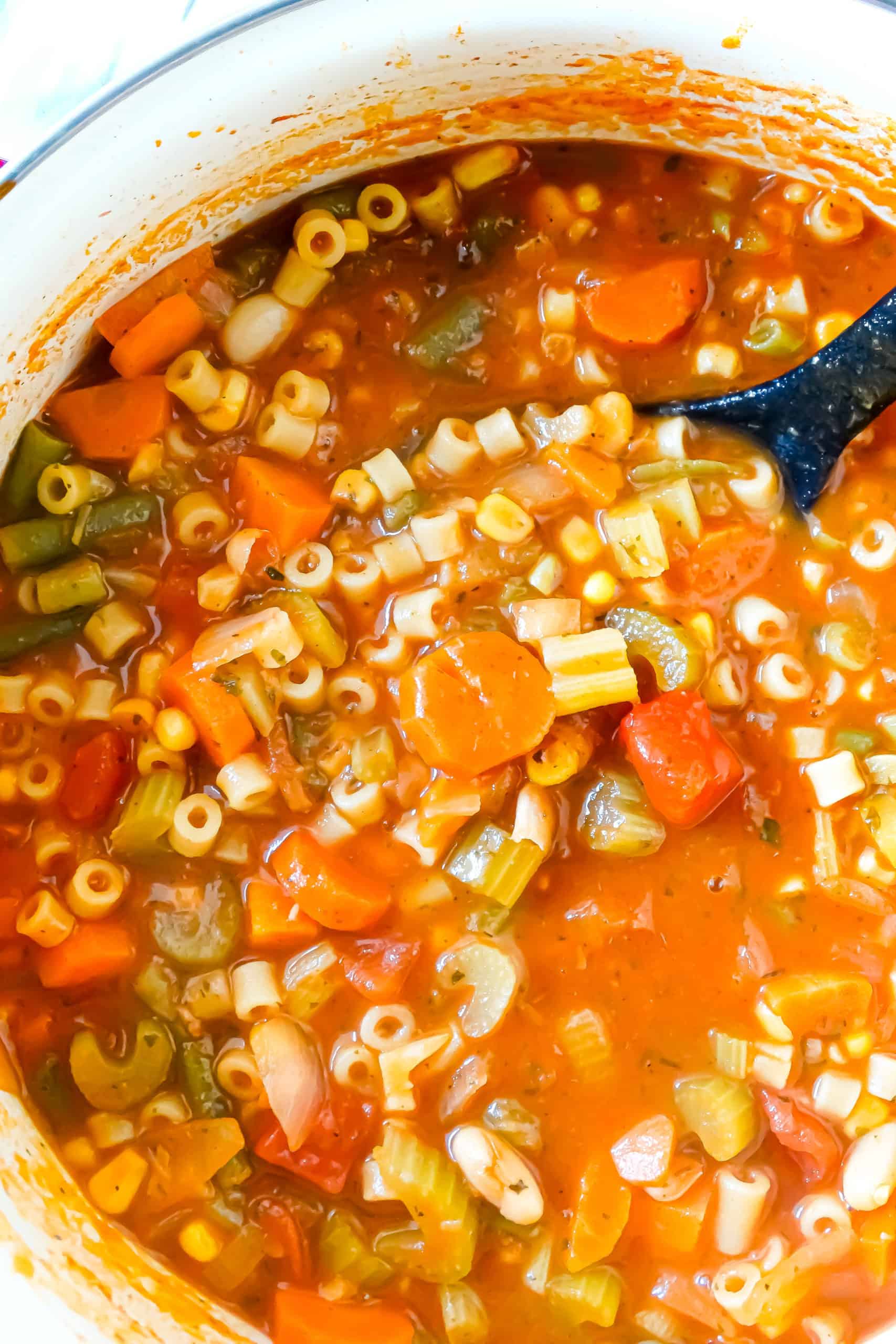 homemade vegetable soup with carrots, celery, white beans, ditalini, green beans, and tomatoes in a large stockpot with a soup ladle.