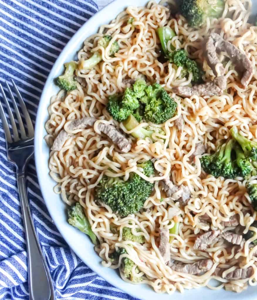 beef broccoli noodles in a grey bowl with fork and napkin
