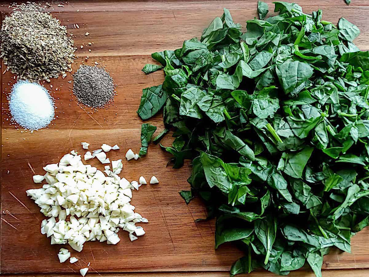 spinach, garlic and spices on a cutting board