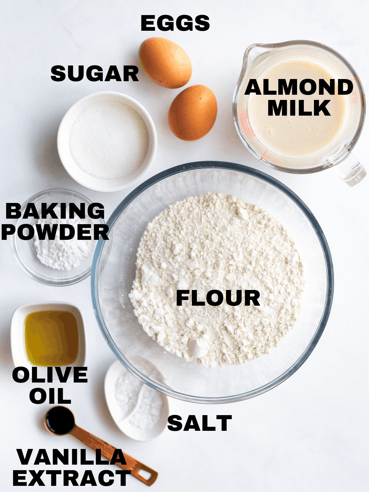 almond milk, flour, salt, extract, baking powder, olive oil, sugar, and eggs on a cutting board
