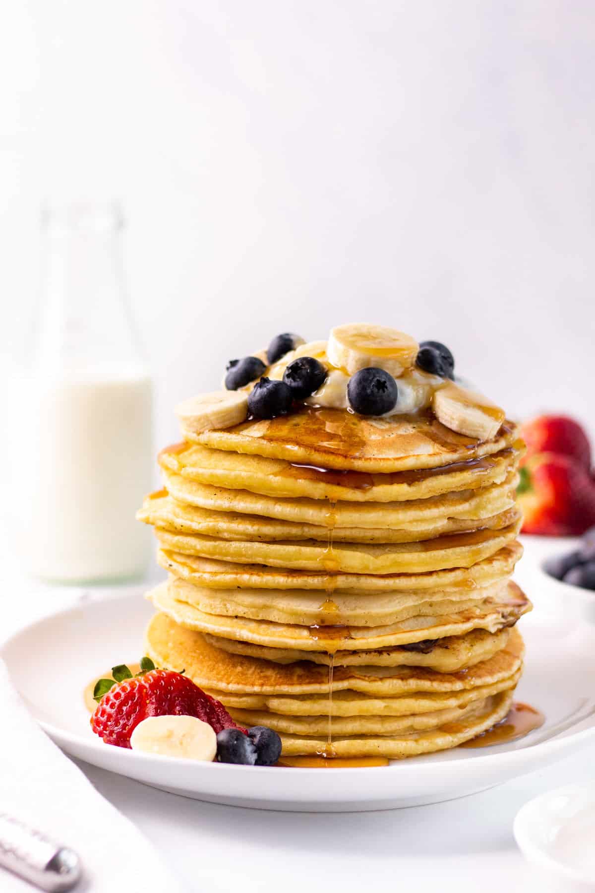 a large stack of almond milk pancakes topped with fruit and syrup