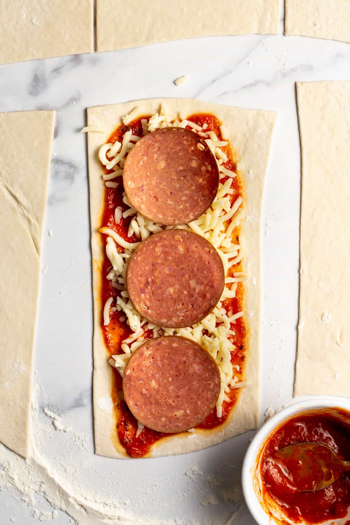pizza dough cut into rectangles and topped with pepperoni, sauce and mozzarella cheese