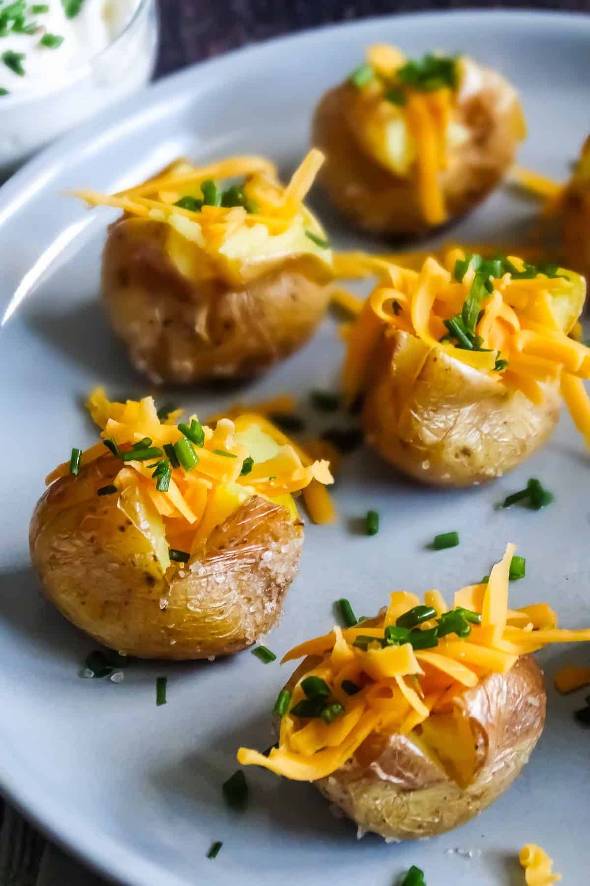 mini baked potatoes with cheddar cheese and chives on a gray plate