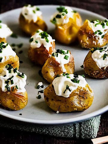 crispy baked mini potatoes topped with sour cream and chives on a plate