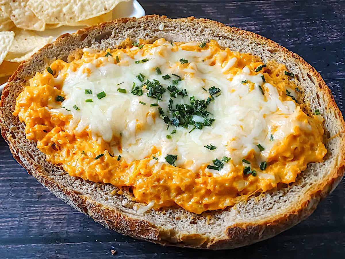 buffalo cauliflower dip in a bread bowl, topped with mozzarella and chives