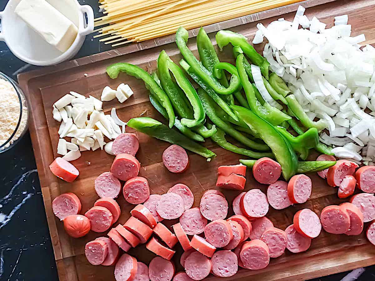 sliced peppers, kielbasa, onions, garlic, and parmesan on a cutting board