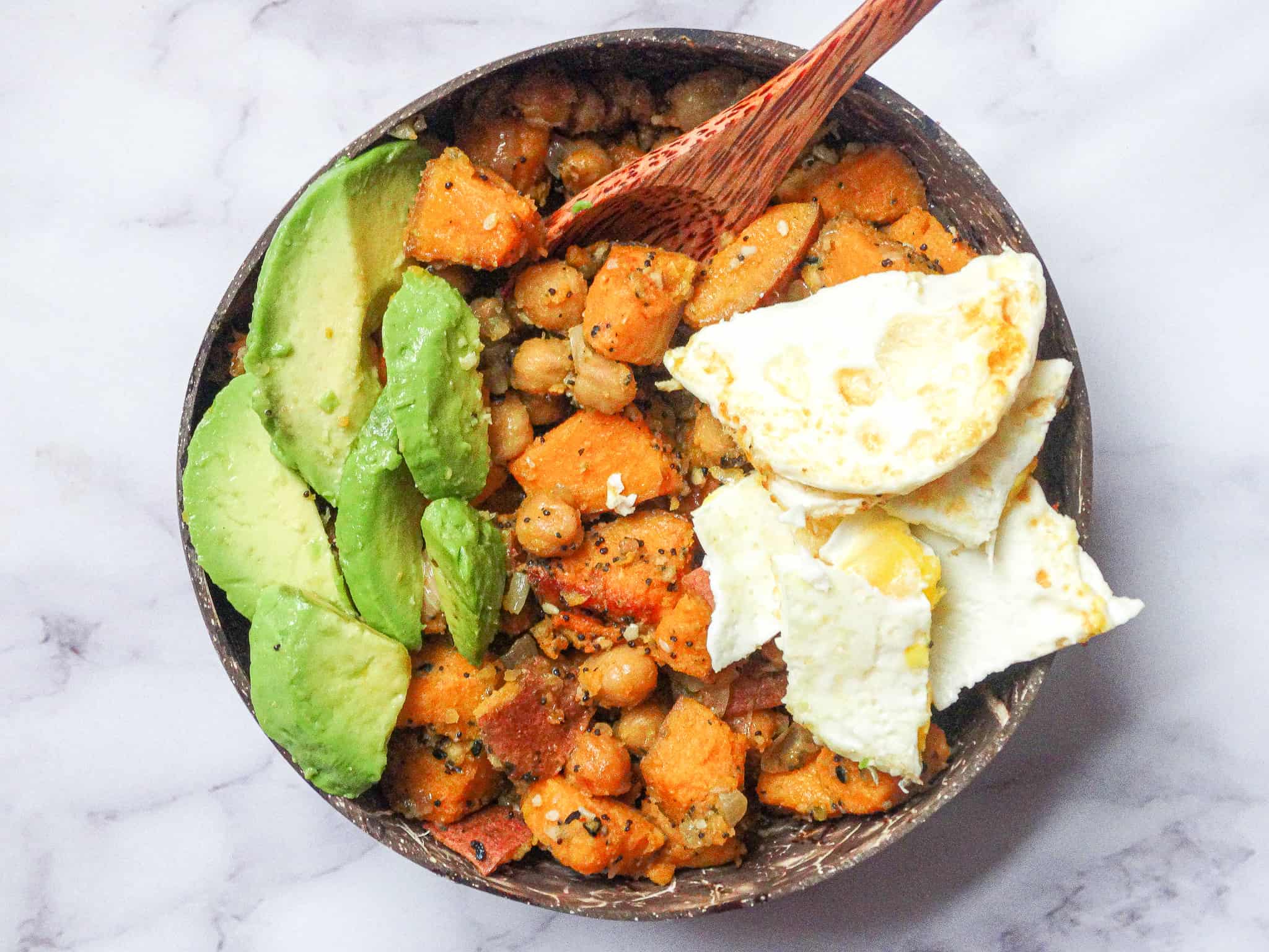 sweet potato chickpea hash with avocado and egg in a coconut bowl