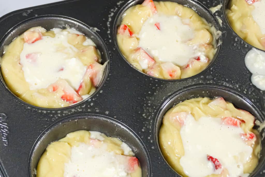 uncooked strawberry muffin batter with cheesecake filling in the center