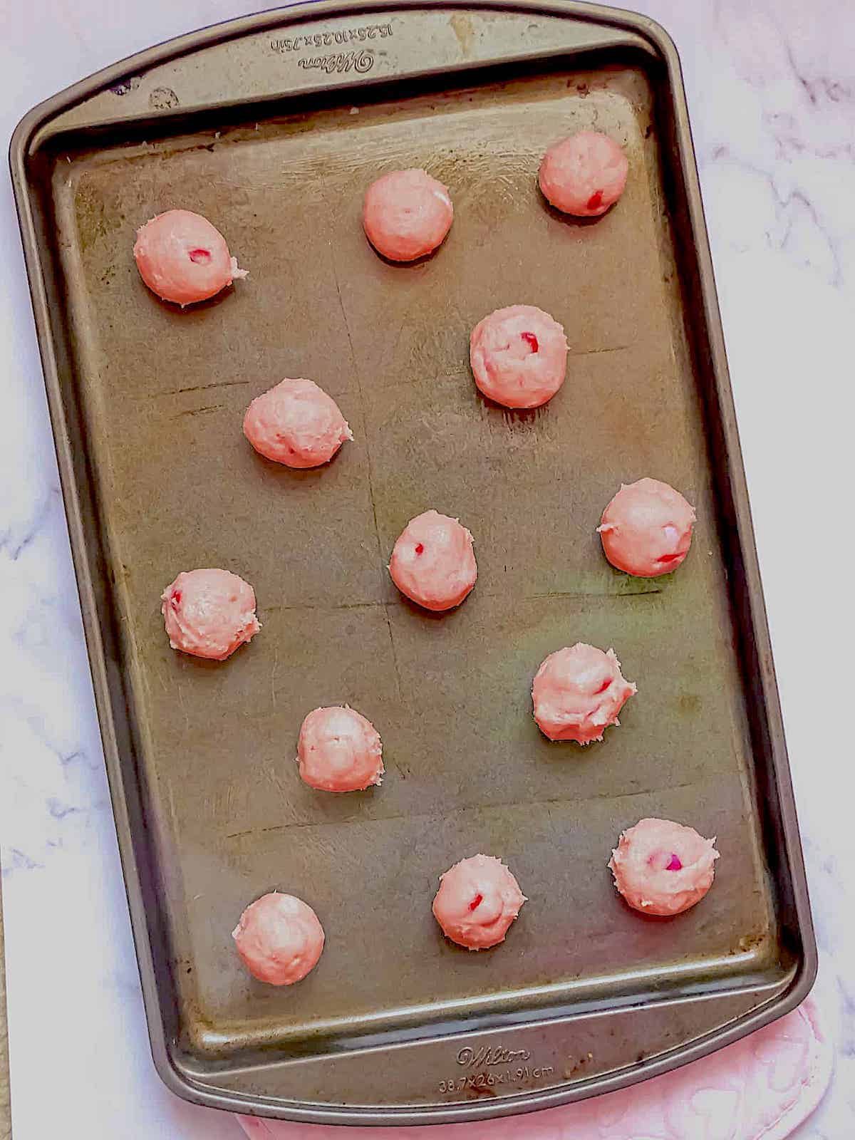 pink sugar cookie dough balls on a baking sheet