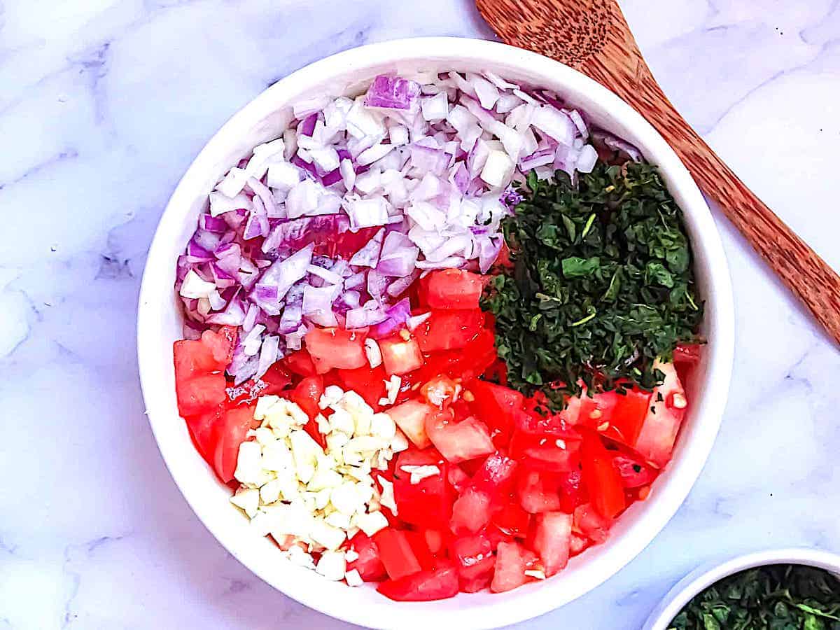 basil, tomatoes, garlic, and red onion in a white bowl