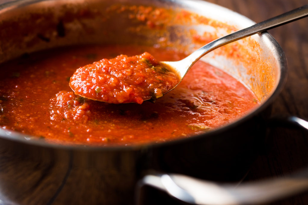 homemade tomato sauce in a spoon lifted out of a pot