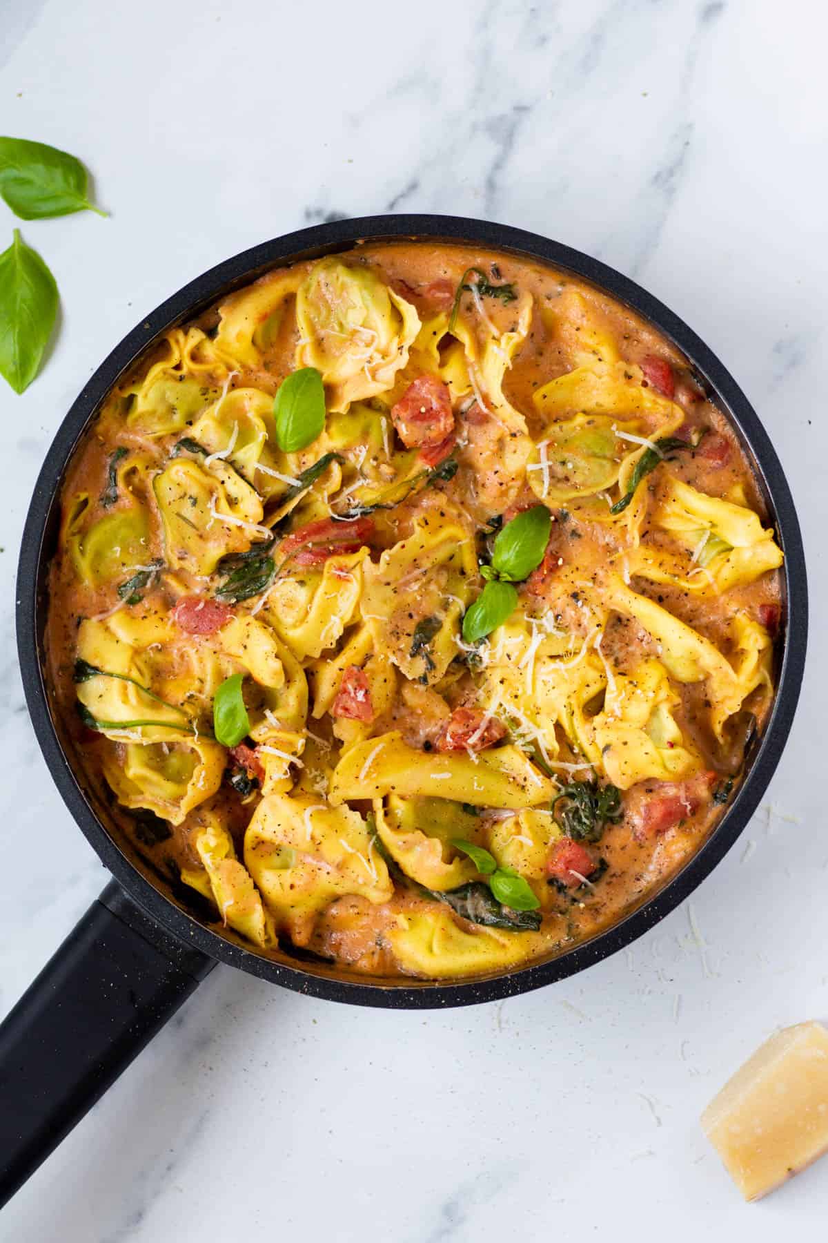 tortellini in cream sauce in a skillet topped with fresh basil