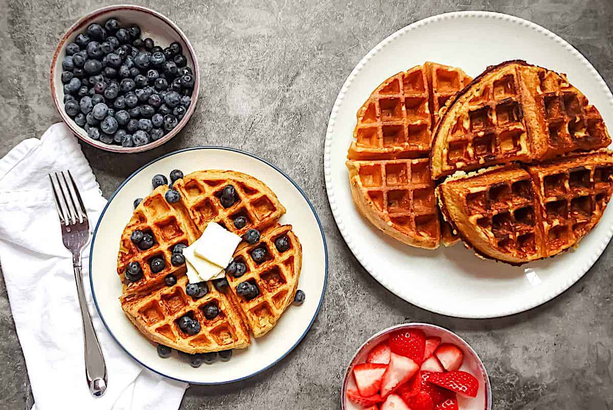 cottage cheese waffles on 2 plates served with a side of strawberries and blueberres