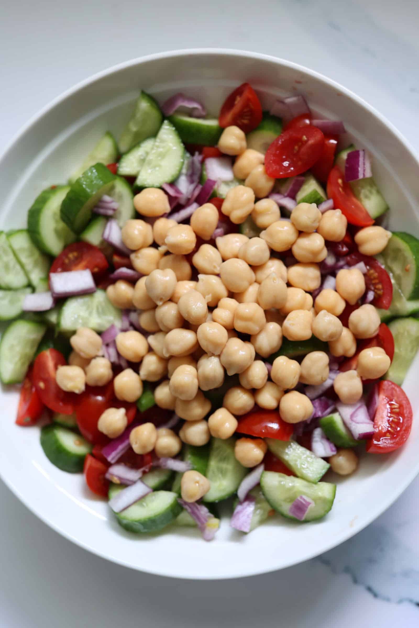 tomato cucumber salad topped with fresh chickpeas in a white bowl