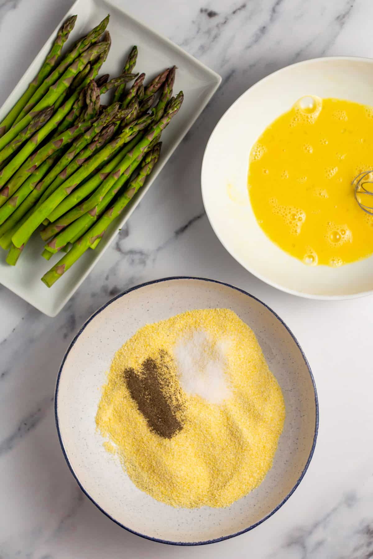 asparagus, a bowl of cornmeal and spices, and a bowl of egg 
