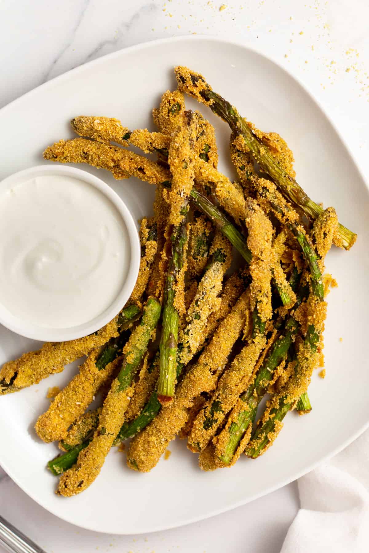 fried asparagus spears on a white plate with a small bowl of dipping sauce