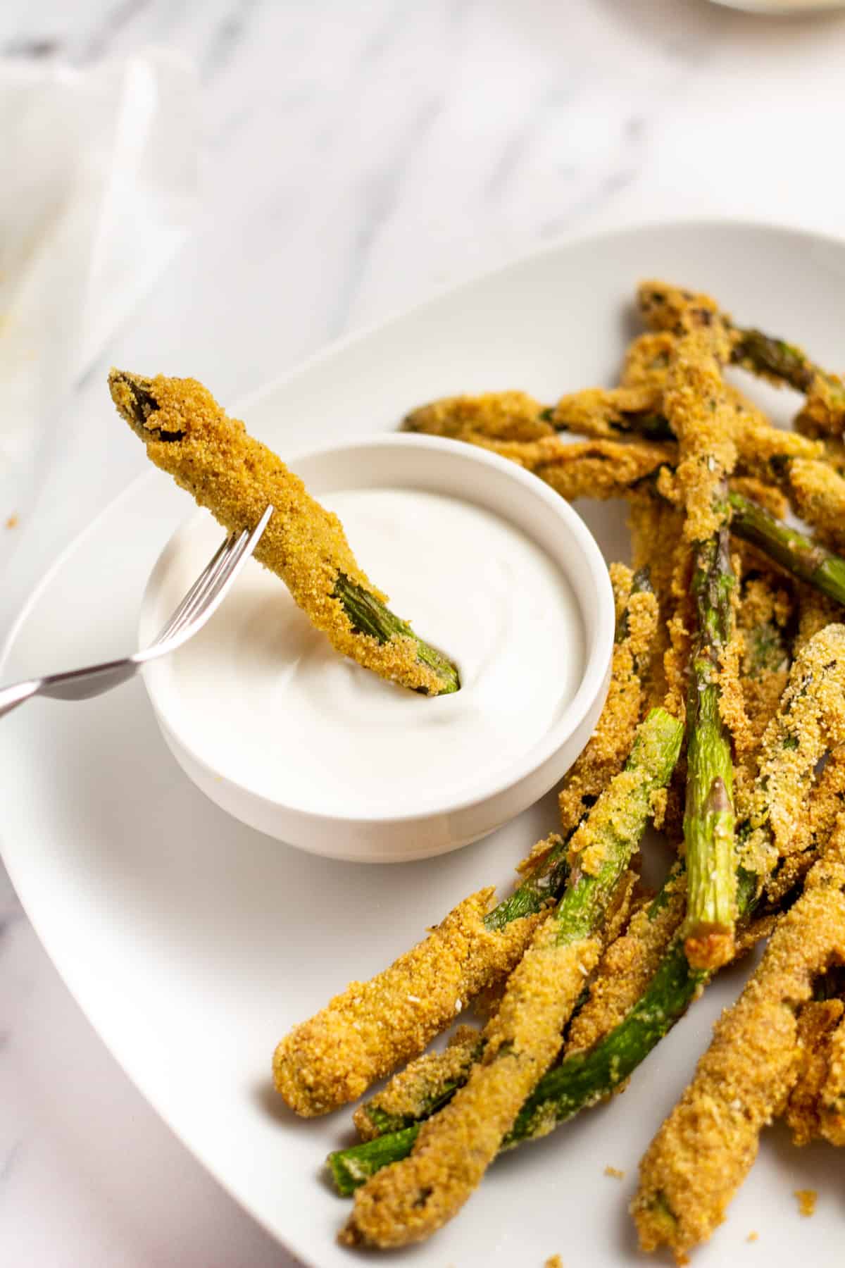 a fried asparagus stick being dipped into a white creamy sauce