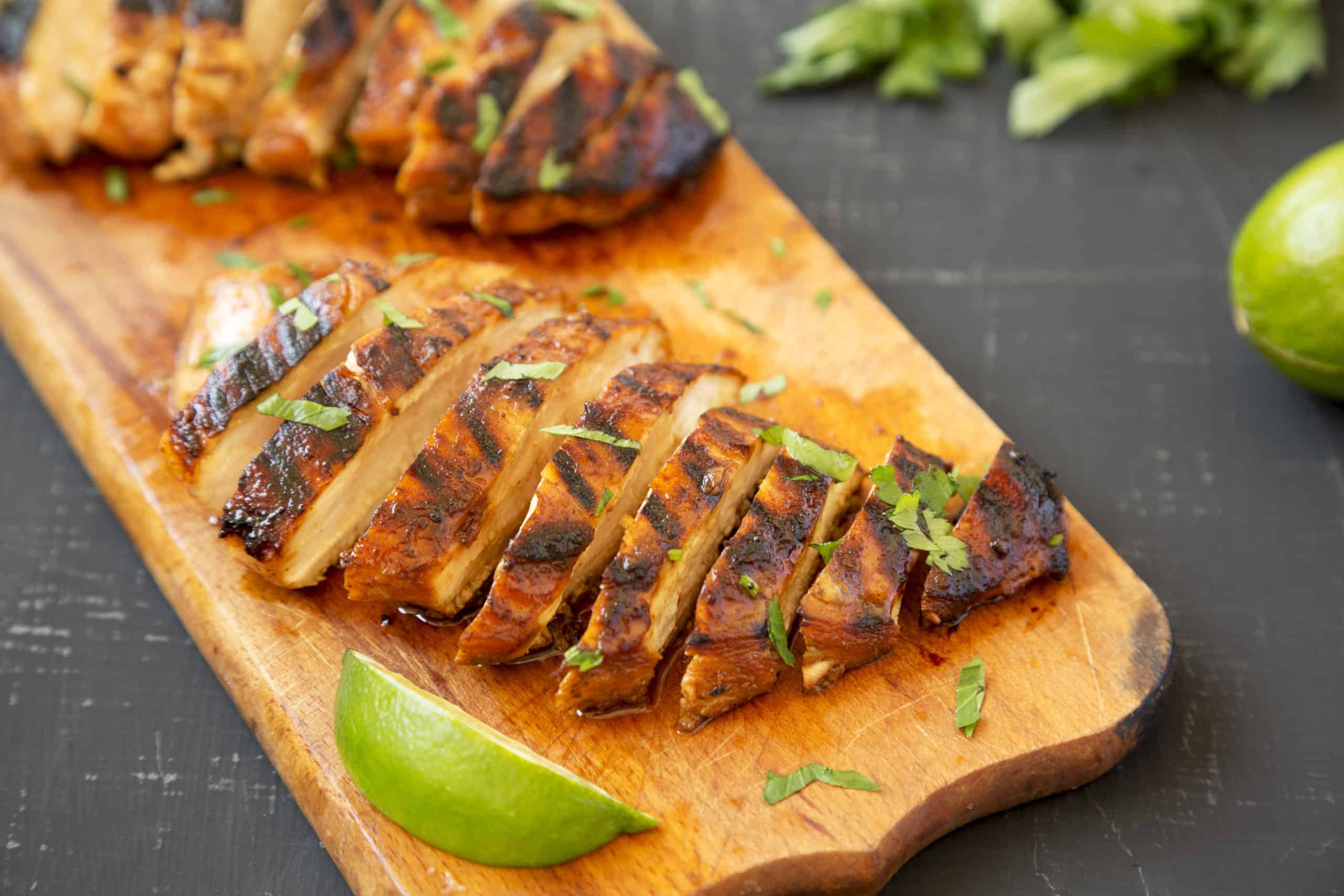 grilled lime chicken with cilantro and lemon sliced on a cutting board and surrounded by limes