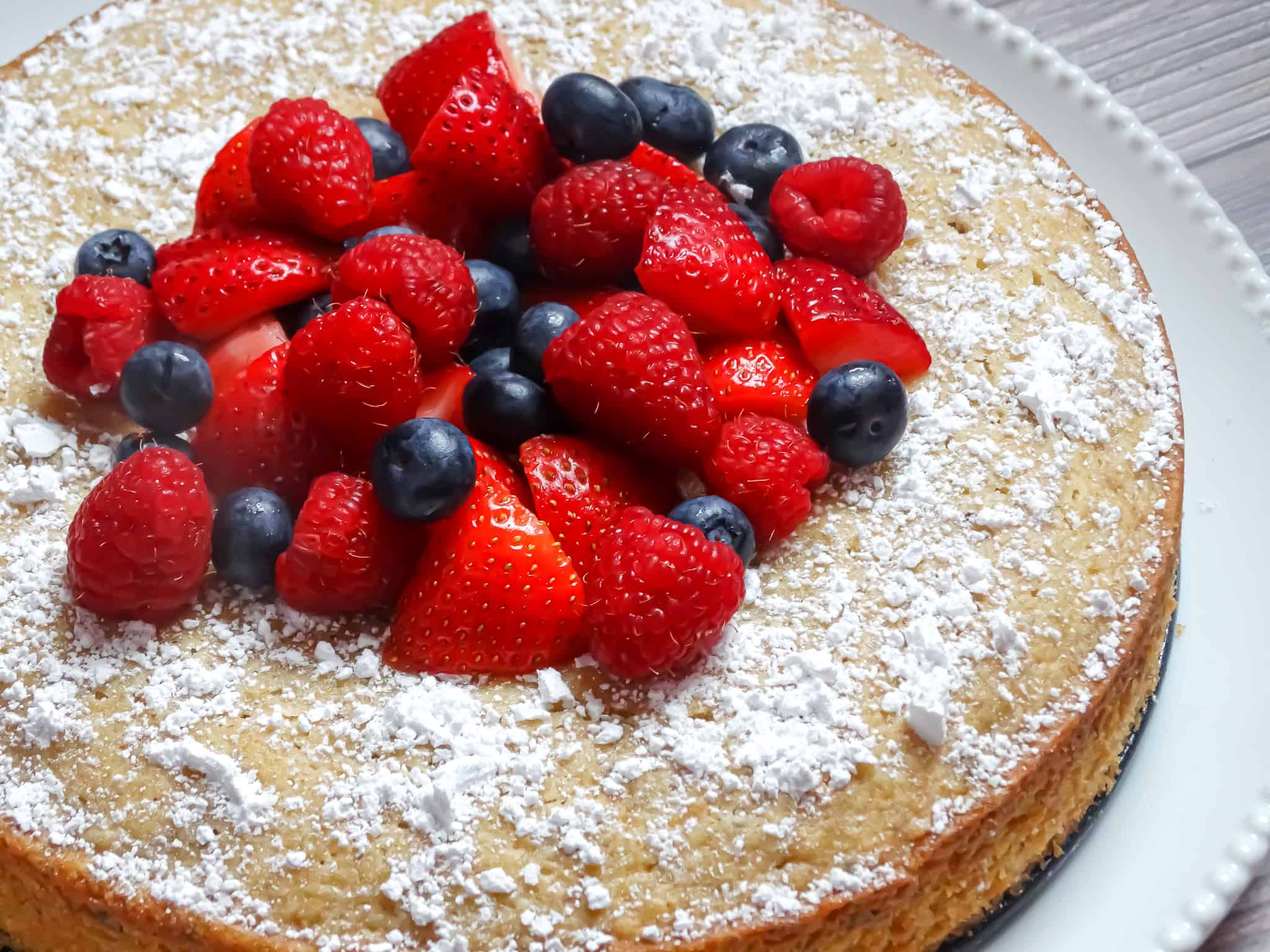 lemon olive cake topped with mixed berries and sprinkled with powdered sugar