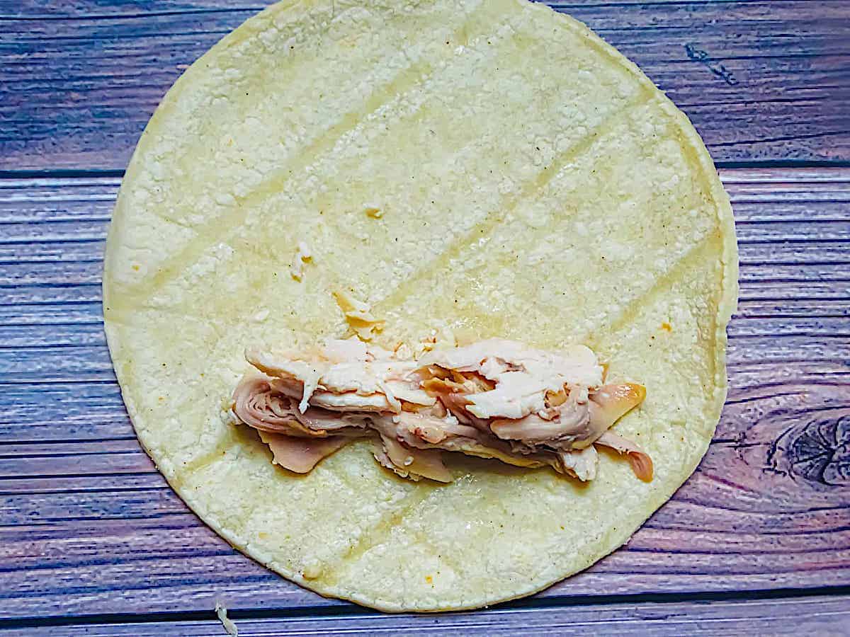 a tortilla shell topped with chicken and cheese to make a taquito
