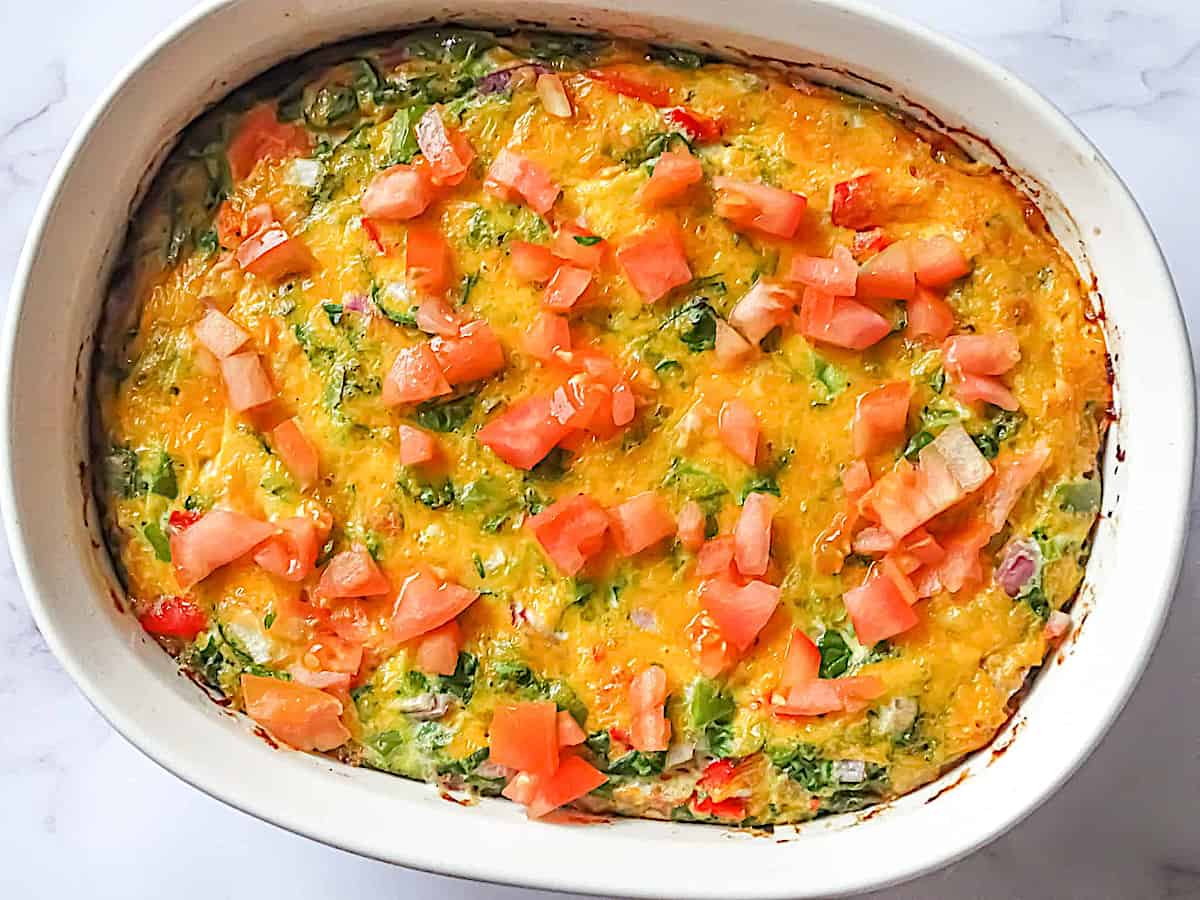 oven baked garden veggie omelette in a casserole pan topped with cheddar and tomatoes