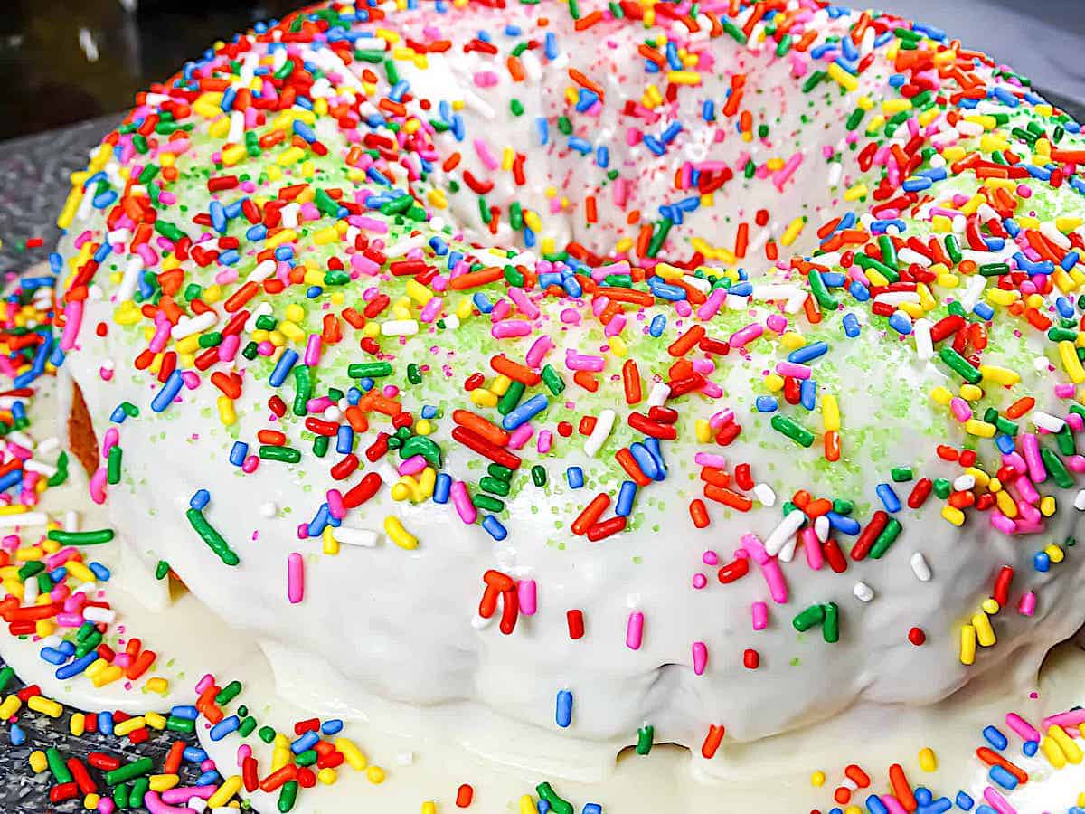 rainbow bundt cake glazed with vanilla icing and sprinkles