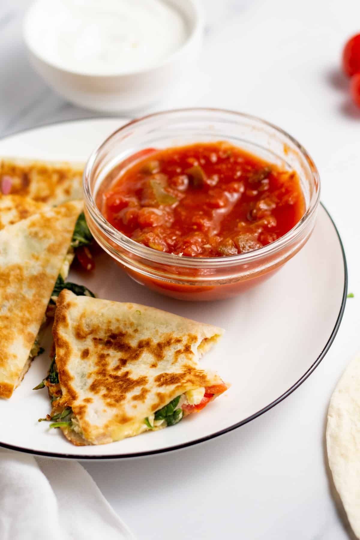 mediterranean quesadilla on a plate with salsa and a bit taken out of 1 piece