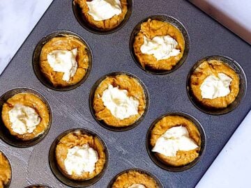 pumpkin muffin batter topped with cream cheese in a muffin tin