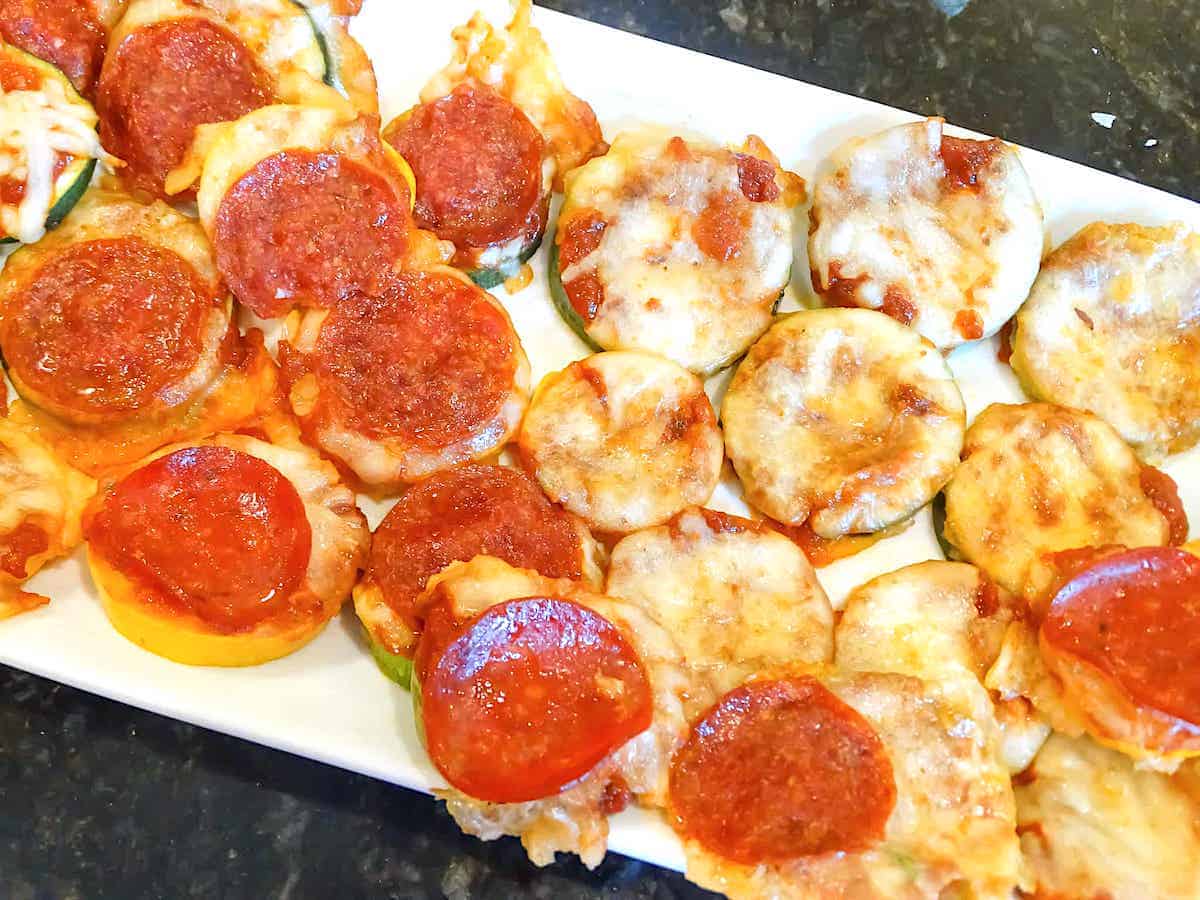 zucchini pizza bites, half with pepperoni and half without on a white plate
