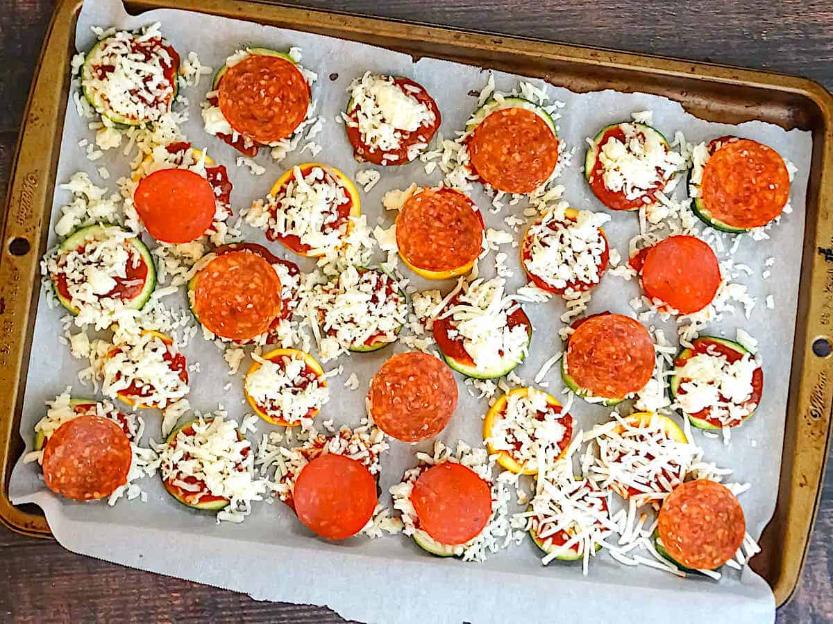 zucchini slices topped with mozzarella and pepperoni on a baking sheet
