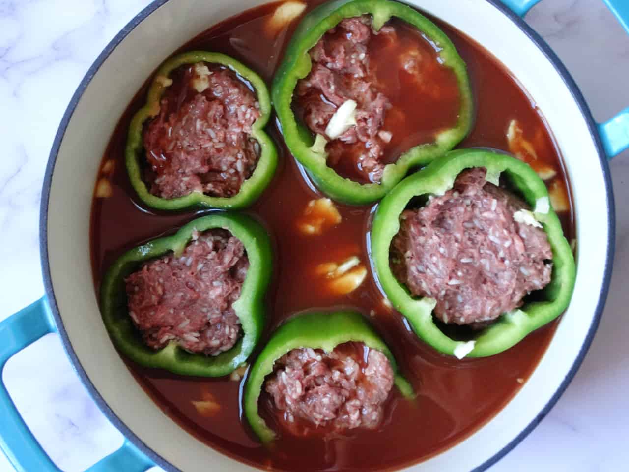 middle eastern stuffed peppers in a large dutch oven covered in tomato broth
