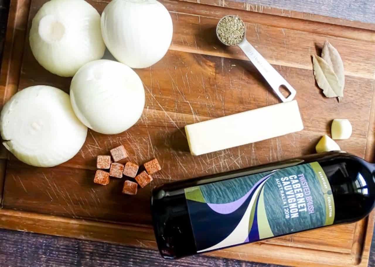 ingredients in French Onion Soup on a cutting board: onions, wine, thyme, garlic, bay leaves, and butter.
