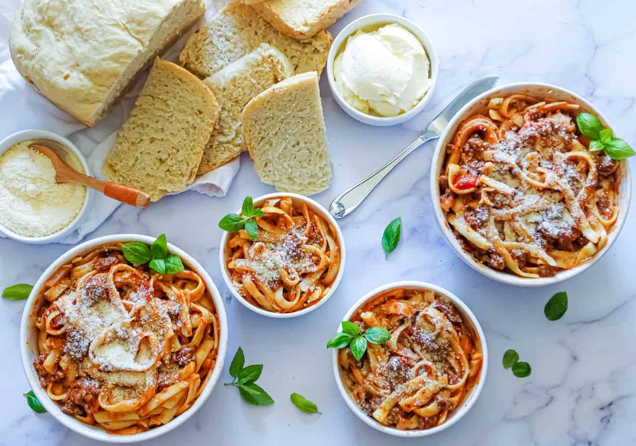 INSTANT Pot spaghetti in 4 bowls topped with parmesan cheese and basil leaves on a white background with garlic bread