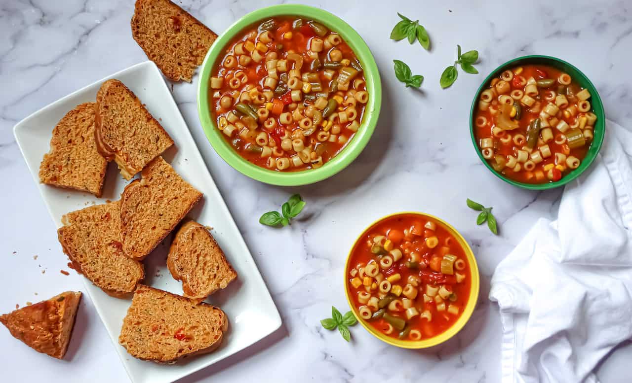 instant pot vegetable soup in kids and adult bowls served with tomato  basil bread on a white background