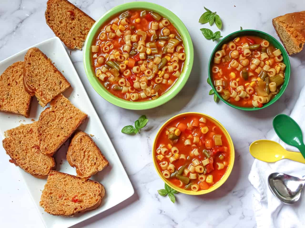instant pot vegetable soup in kids and adult bowls served with tomato basil bread on a white background