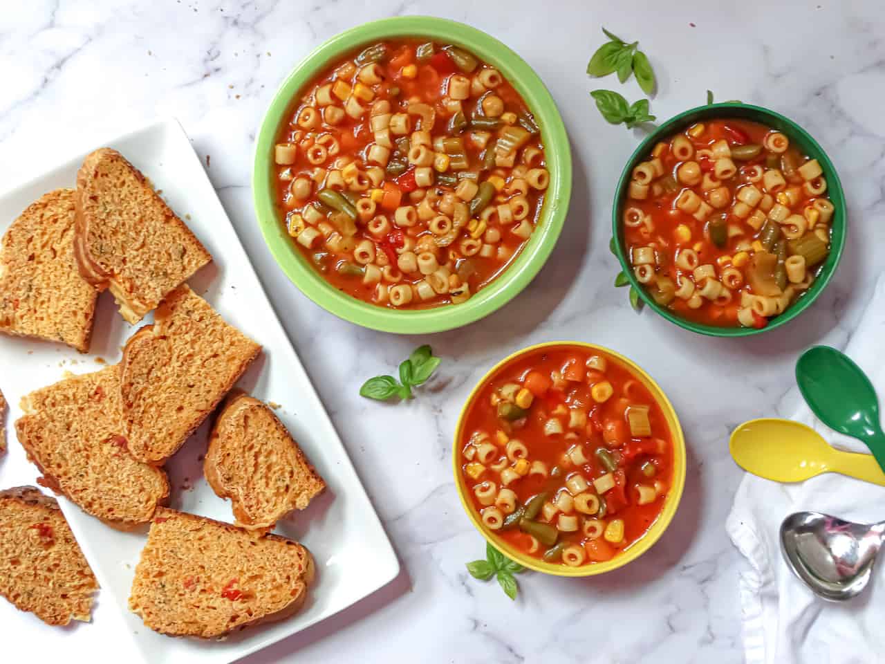 instant pot vegetable soup in kids and adult bowls served with tomato basil bread on a white background