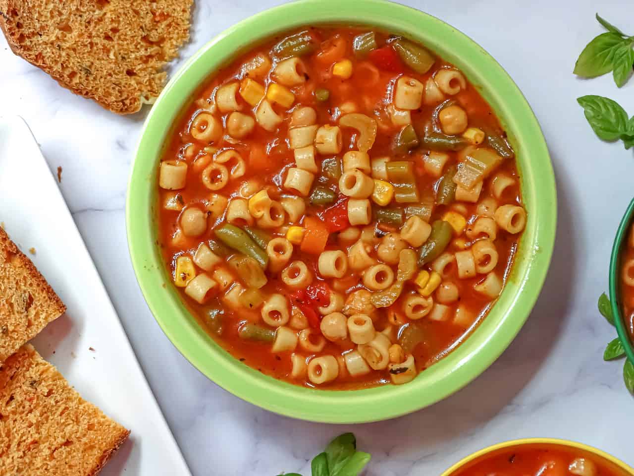 instant pot vegetable soup in a green adult bowl served with tomato  basil bread on a white background