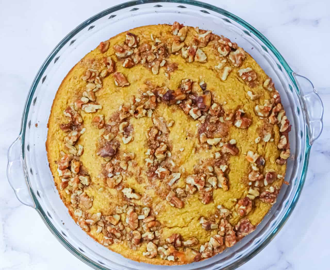 cooked pumpkin cornbread with walnut topping in a pie plate on a white background