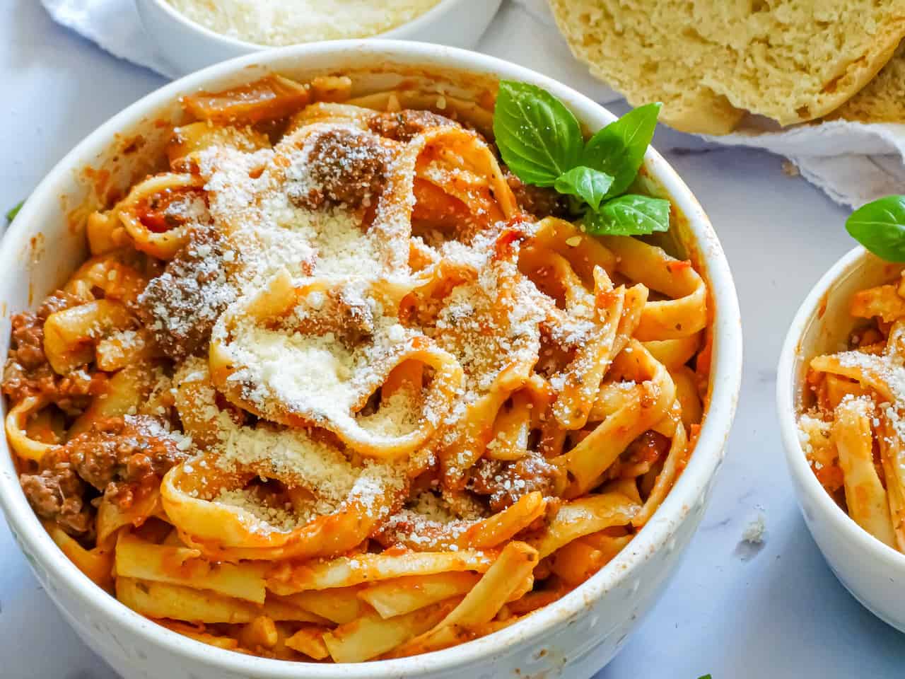 instant pot spaghetti and meat sauce in a white bowl topped with parmesan cheese and basil leaves