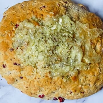 a loaf of baked brie cranberry bread on a white cutting board