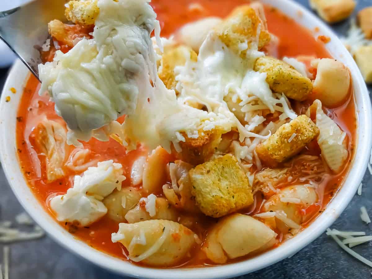 easy chicken parmesan crockpot soup in a white bowl topped with croutons, shredded parmesan and fresh mozzarella