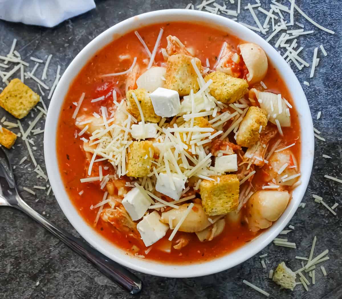easy chicken parmesan crockpot soup in a white bowl topped with croutons, shredded parmesan and fresh mozzarella