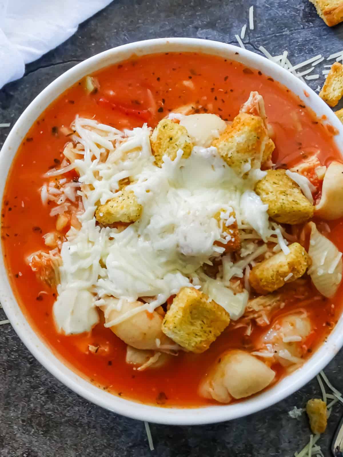 slow cooker chicken parmesan soup in a white bowl topped with croutons and cheese