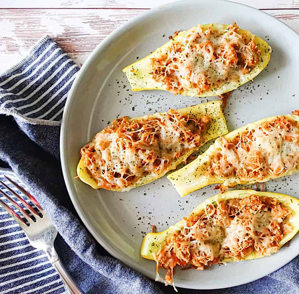 Cheesy roasted squash boats on a white plate with a serving napkin and fork