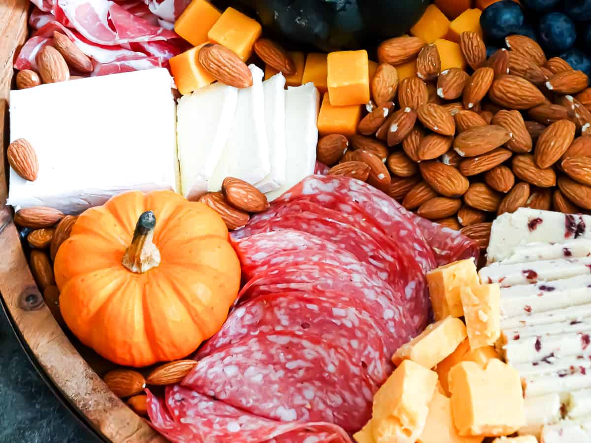 Meats, cheeses, fruits, nuts, and spreads arranged on a circular board intended to be an easy Thanksgiving appetizer